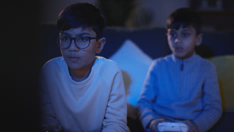 Front-View-Of-Two-Young-Boys-At-Home-Having-Fun-Playing-With-Computer-Games-Console-On-TV-Holding-Controllers-Late-At-Night-3